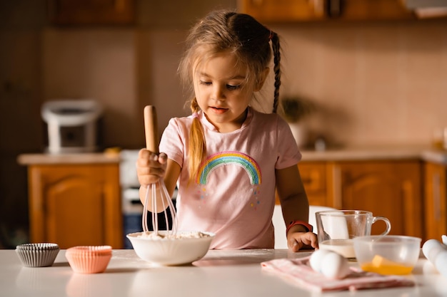 Cute little blonde girl cooking dough in kitchen at home