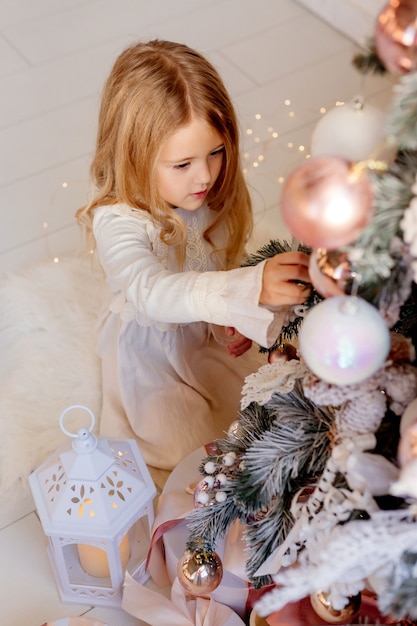 Cute little blonde girl in dress near Christmas tree