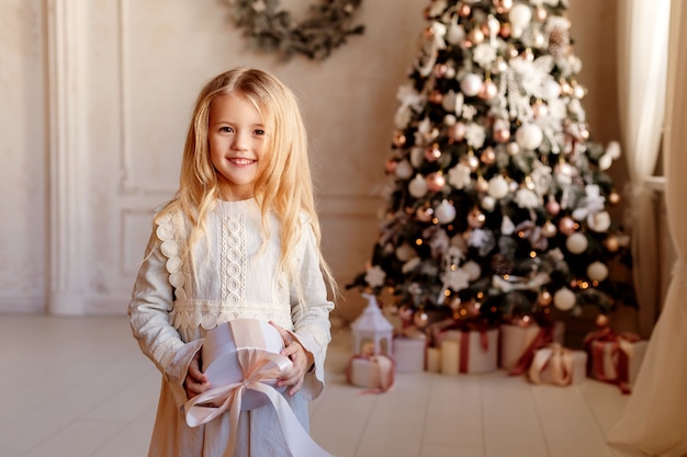 Cute little blonde girl in dress near Christmas tree