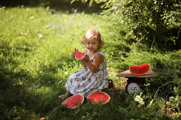 かわいいブロンドの女の子は通りで夏に新鮮な赤いスイカを食べます