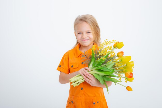 Cute little blonde girl in  holding a bouquet of spring flowers on a white background