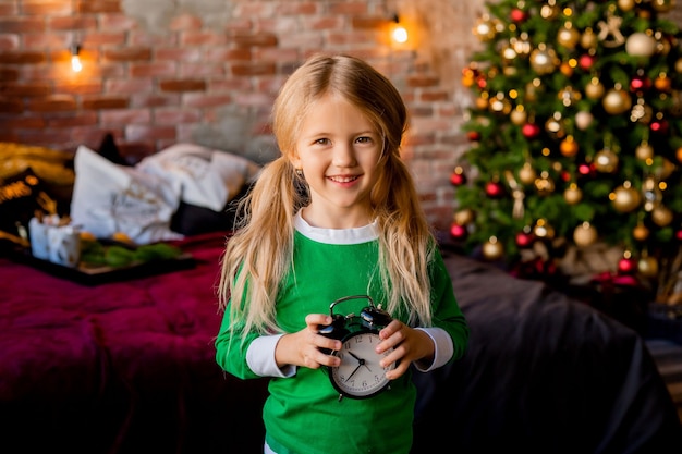 Cute little blonde girl in pajamas near Christmas tree