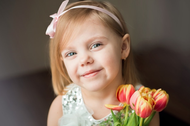 Cute little blonde girl of three years with peach tulips close up and smiling, her hair on her shoulders