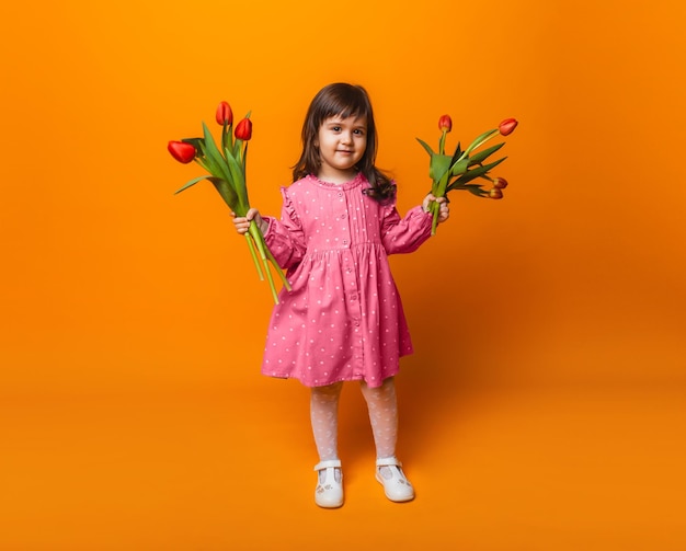 Cute little blonde girl with a bouquet of tulips in a cotton dress on a pink background March 8