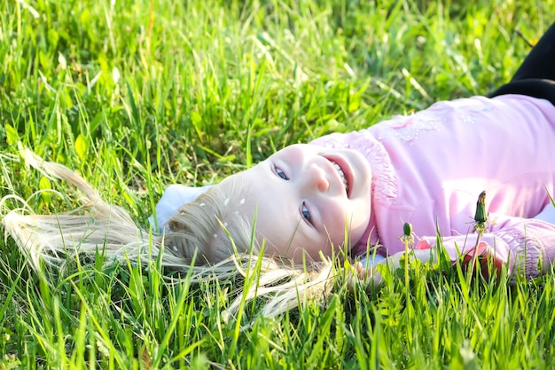 Cute little blonde girl with white petals of bird cherry tree on her hair lying on the green meadow in spring park