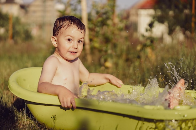 Cute little boy bathing in tub outdoors in garden Happy child is splashing playing with water and having fun Summer season and recreation Staying cool in the summer heat Water fun in backyard