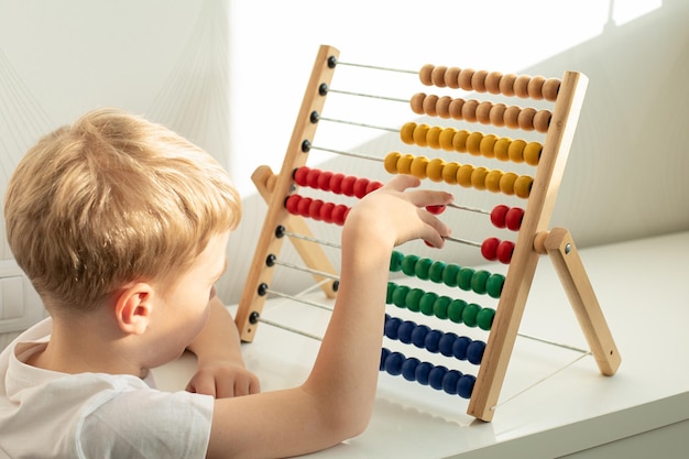 Un simpatico ragazzino biondo è impegnato con banconote di legno colorate giochi montessori educazione concettuale