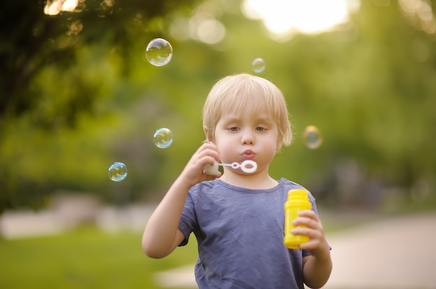 Cute little boy blowing soap bubbles in beautiful summer park.