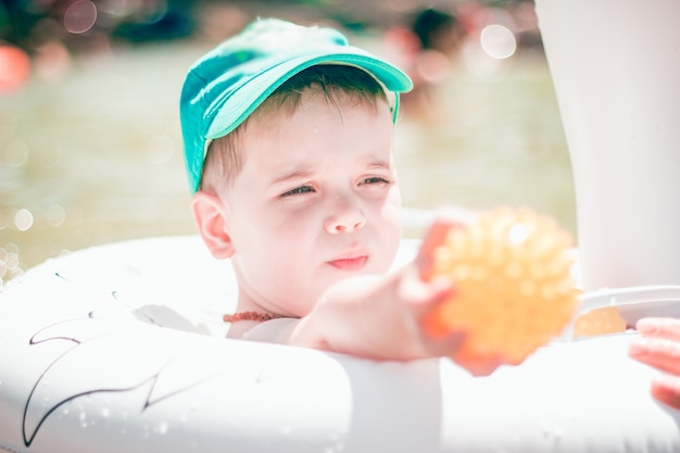 A cute little boy in a blue baseball hat swimming in the sea in an inflatable ring.