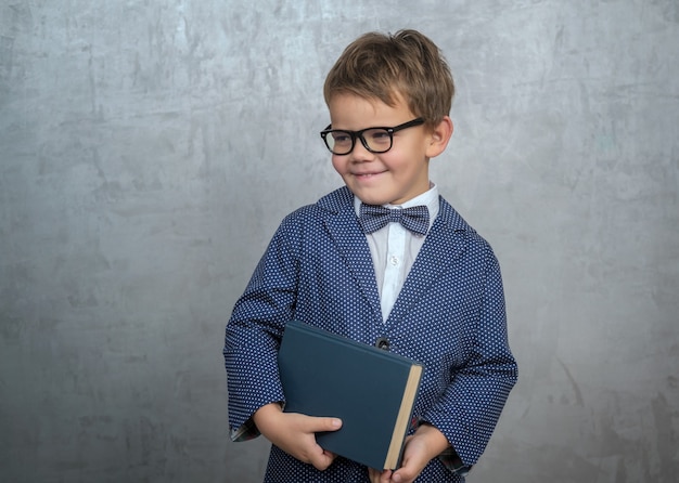 Cute little boy in dark glasses, stylish jacket with a butterfly and a book in his hands.