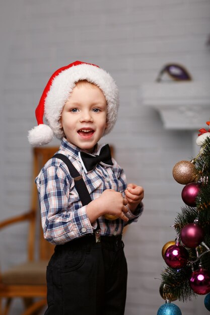 かわいい男の子は、クリスマスの装飾でインテリアのクリスマスツリーを飾ります