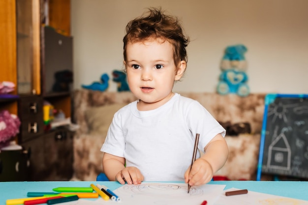 A cute little boy draws in his sketchbook with colored pencils