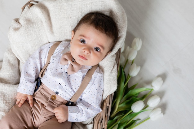 Cute little boy dressed up laying in basket with white tulips card banner