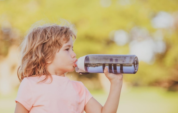 Cute little boy drink water from sport bottle in green park closeup portrait of sporty child exercis