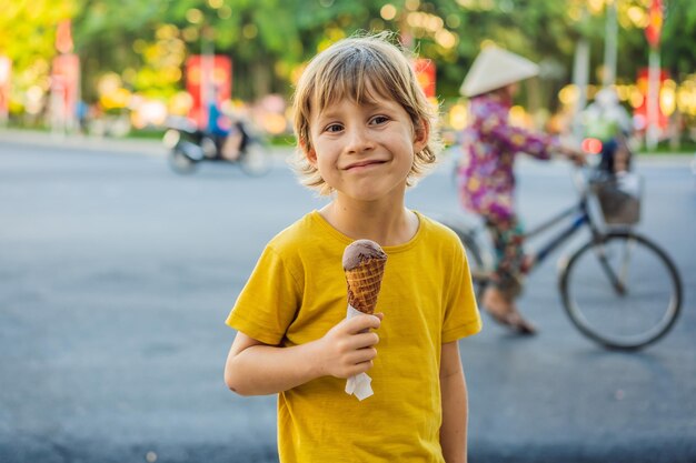 Cute little boy eating big ice cream in the park smiling at camera summertime