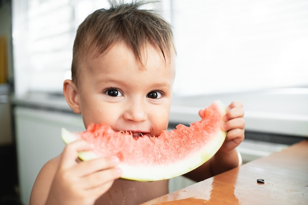 Cute little boy eating watermelon in the kitchen, very cute