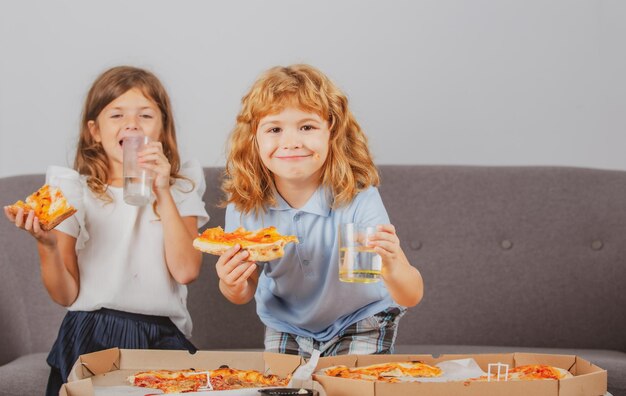 Foto ragazzino e ragazza svegli che mangiano pizza a casa i bambini che tengono le fette di pizza sulla festa a casa li