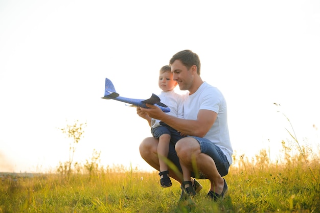 Cute little boy and his handsome young dad are smiling while playing with a toy airplane in the park