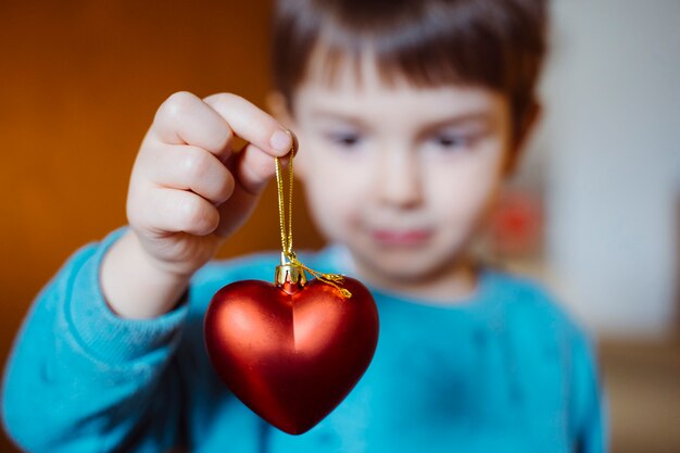 Cute little boy holding with cheerful smile a red shaped heart on her living room