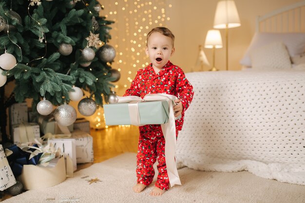 プレゼントを探している大きなクリスマスツリーのそばに家にいるかわいい男の子。幸せな子供は休日に時間を過ごし、すべての瞬間を楽しんでいます。一人で家。