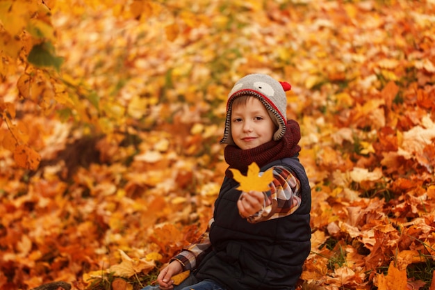 Cappello infunny del ragazzino sveglio e sciarpa calda all'autunno dorato in parco.