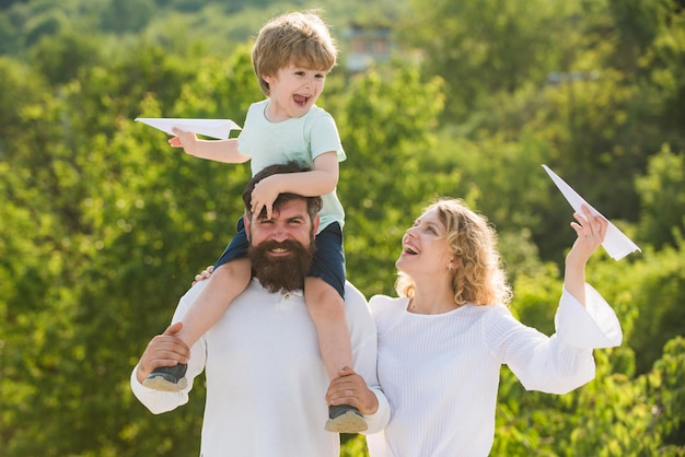 Cute little boy is holding paper airplane Family like summer time together Father mother and son in the park Summer ration Parenthood