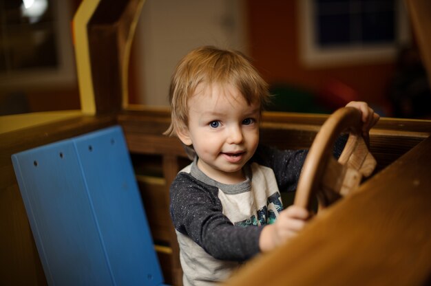 かわいい男の子はおもちゃの木製の車で遊んでいます