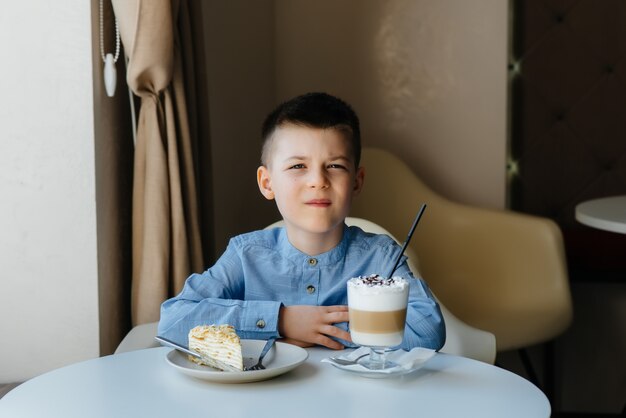 かわいい男の子がカフェに座って、ケーキとココアのクローズアップを見ています。食事と適切な栄養。