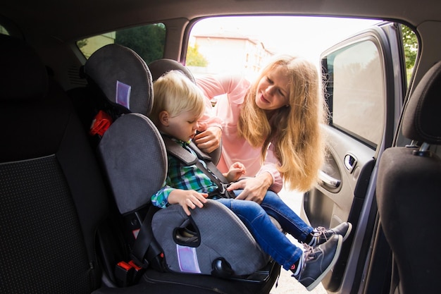 The cute little boy is sitting in a car seat Mom fastens her baby who is sitting in the car