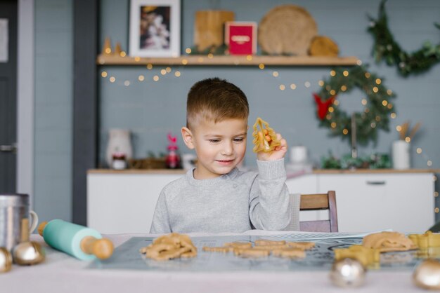 A cute little boy is sitting at the table and preparing\
christmas cookies family vacation at home during the holidays new\
year and christmas