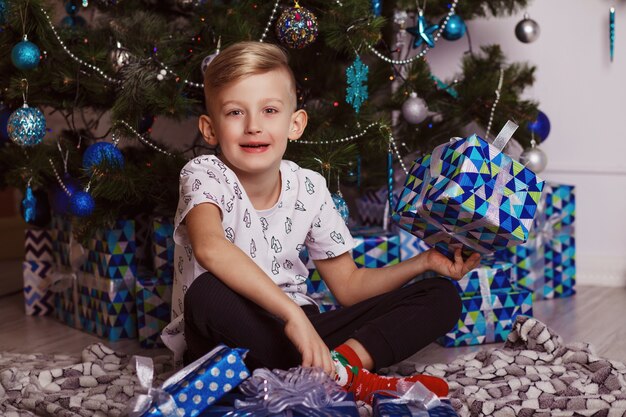 Cute little boy is sitting with a gift near the Christmas tree.