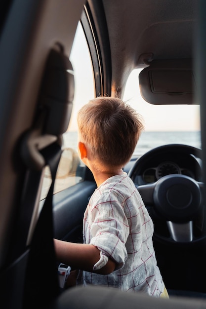 Cute little boy looking out of window of a car during sunset on the beach