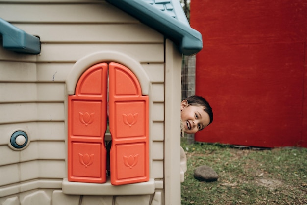 A cute little boy looks out of a toy house little boy with dark hair plays a game of hide and seek