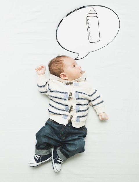 Cute little boy lying on bed and dreaming of bottle with milk