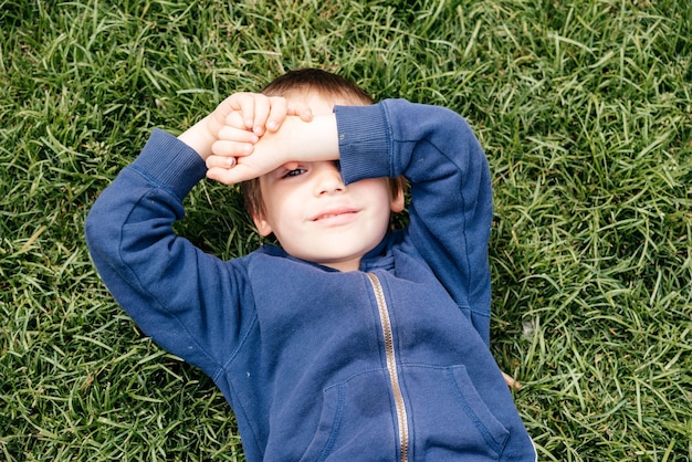 Cute little boy lying on green grass in park