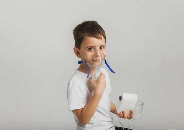 Photo cute little boy makes inhalation. the child holds an inhaler in his hand and is being treated for a cough. high quality studio photo.