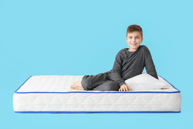 Cute little boy on mattress against color