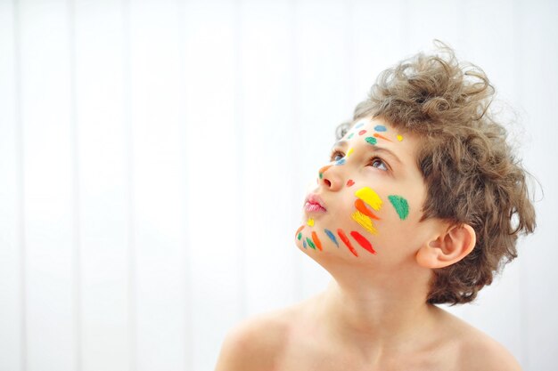 Photo a cute little boy painted colorful stripes on his face with paints