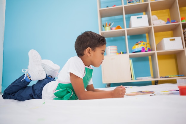 Cute little boy painting on floor in classroom