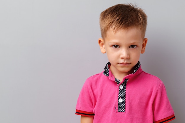 Cute little boy in pink T-shirt posing against grey background