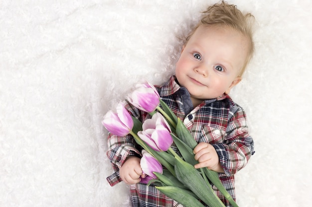 Cute little boy in a plaid shirt holds a bouquet of pink tulips