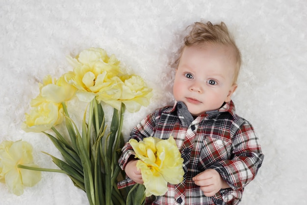 格子縞のシャツを着たかわいい男の子が黄色のチューリップの花束を保持しています。