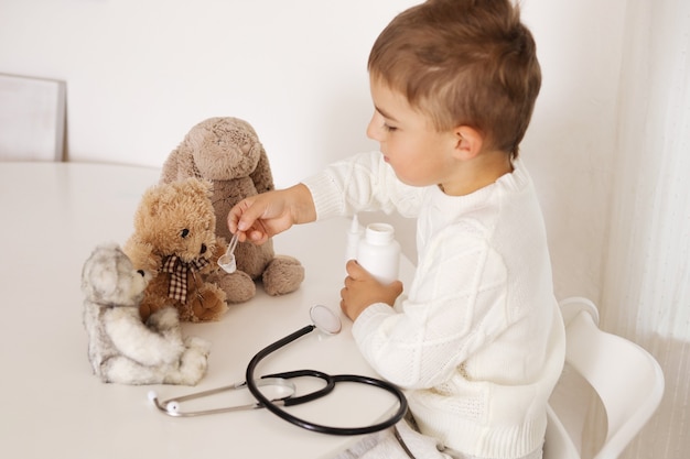 Cute little boy playing doctor at home and curing plush toy. Sweet toddler child plays indoor. Having fun. Kids and medicine, healthcare.