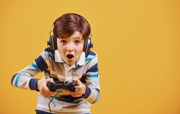 Cute little boy playing video game in the studio against yellow background.