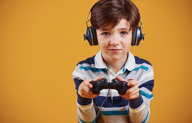 Cute little boy playing video game in the studio against yellow background.