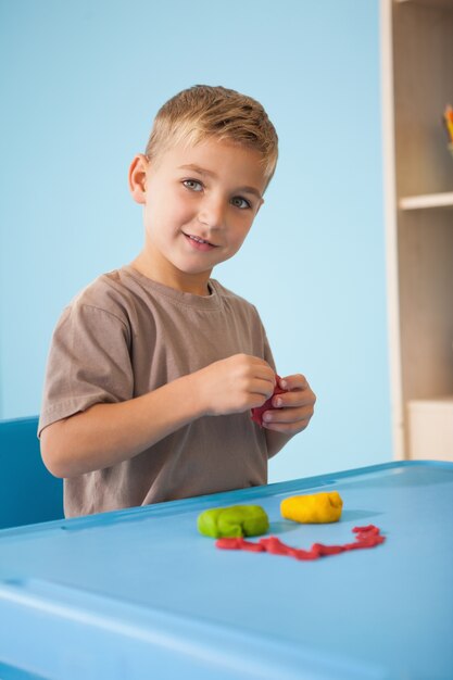 Cute little boy playing with modelling clay in classroom