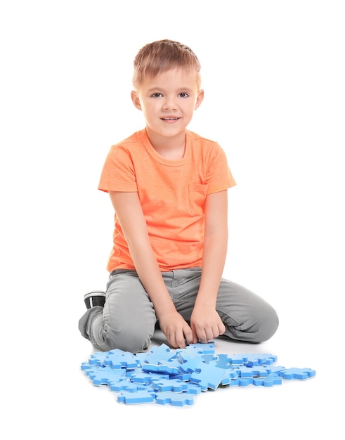 Cute little boy playing with puzzle on white background