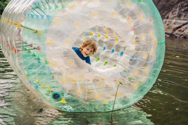 Cute little boy playing in Zorb a rolling plastic cylinder ring with a hole in the middle on the lake