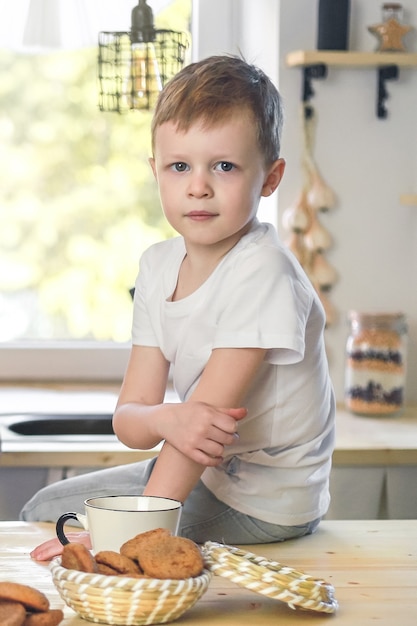 キッチンルームで木製のテーブルの朝食に座っている白いTシャツのかわいい男の子の肖像画