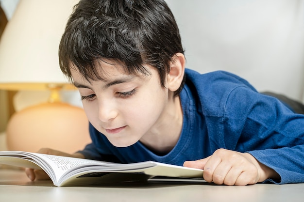 Cute little boy reading book under a tent at home alone